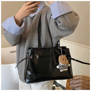 Selfie allo specchio di una borsa tote in vernice nera con ciondolo a orsetto e fibbia