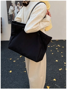 Close-up of a large black canvas tote bag carried by a model in a late autumn outdoor setting