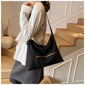 Detail of black tote bag with gold zipper pocket shown on a model in minimalist interior