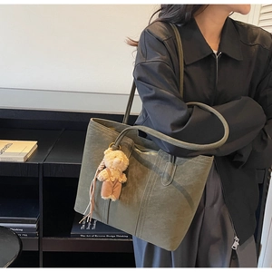 Detailed view of an olive green suede tote bag featuring a cute teddy bear charm and stitching