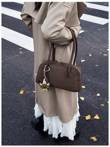 Detail of dark brown suede shoulder bag with cute bear charm on autumn city street