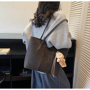 Dettaglio borsa tote marrone scuro con ciondolo a orsetto e nappe in ambiente moderno