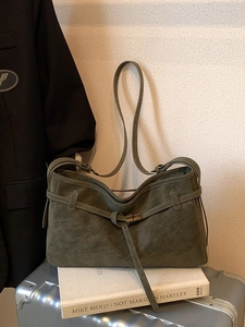 Sac fourre-tout vert olive en daim avec fermoir doré sur fond de livres blancs