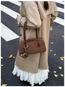 Detail of a brown suede Boston bag with plush bear charm and star tag in autumn street setting
