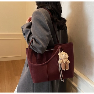 Detail view of large burgundy suede tote bag with a cute plush bear charm on a strap