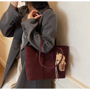 Detail of burgundy matte suede tote bag featuring a cute brown plush bear charm