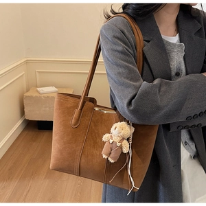 Close-up of brown suede tote bag with reinforced seams and a cute bear plush pendant