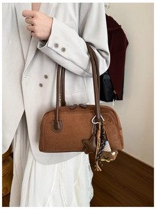 Close-up of brown suede cylindrical handbag with leather handles and bear pendant charms