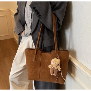 Close-up of brown suede tote bag featuring fine stitching and a cute bear charm detail