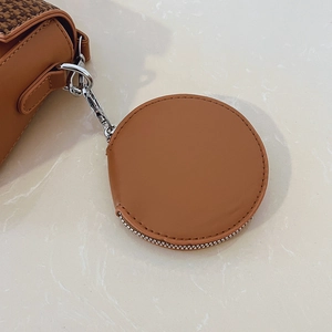 Detail of round coin purse pendant with silver clasp on houndstooth crossbody bag