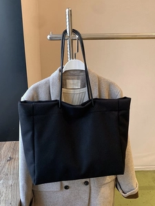 Minimalist large black canvas tote bag hanging on a display stand with a grey coat