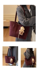 Dettaglio della borsa tote in pelle bordeaux con ciondolo a forma di orsetto di peluche