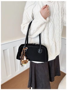 Detail view of black underarm bag with white contrast stitching and a bear keychain
