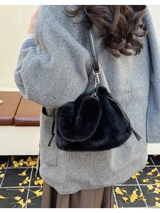 Detail of black faux fur bucket bag featuring a drawstring closure and leather strap