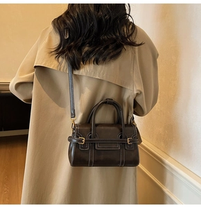 Deep brown leather crossbody bag with white stitching shown on a trench coat