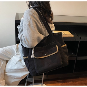 Detail of black corduroy tote bag with side pockets and cotton tassel on zipper