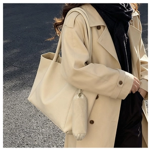 Close-up of beige tote bag with cylindrical pendant held by model in trench coat