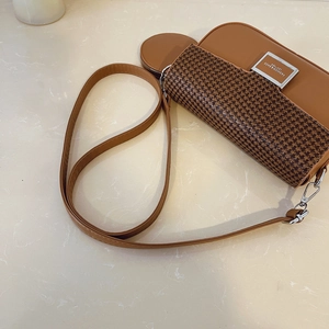 Detail of a brown houndstooth leather crossbody bag with a metal buckle and mini pouch