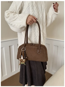 Close-up of a brown Boston bag with contrast white stitching and cute bear charm