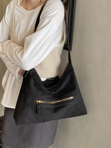 Black suede hobo tote bag with gold zipper detail and long shoulder strap in a stylish pose