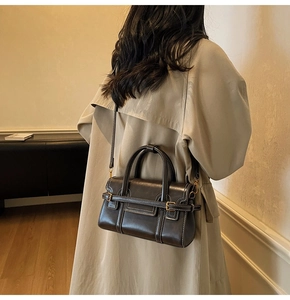 Detail of vintage coffee leather handbag worn with beige trench coat in warm interior