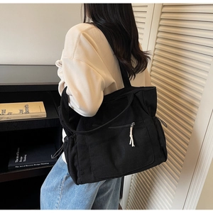 Side view of black corduroy tote bag with drawstring pockets and wide shoulder strap