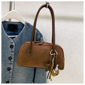 Detail of a brown suede Boston bag featuring long straps and cute bear doll charm