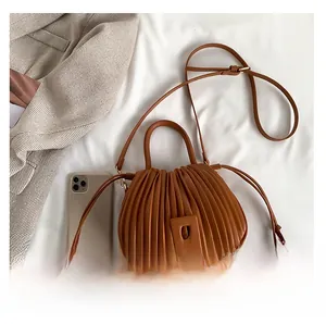 Détail du sac à main marron plissé avec boucle carrée sur fond de tissu blanc texturé