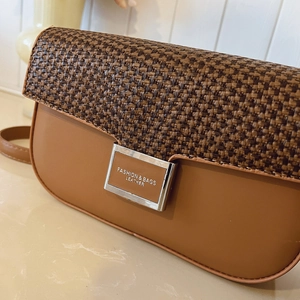 Detail of a brown patchwork crossbody bag with woven texture flap and metallic buckle