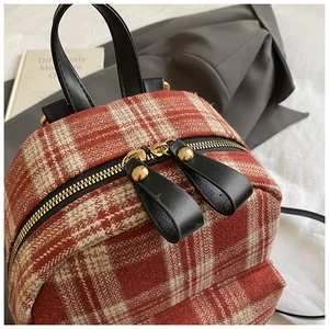 Detail of red plaid tweed backpack with gold dual zippers and black leather handle