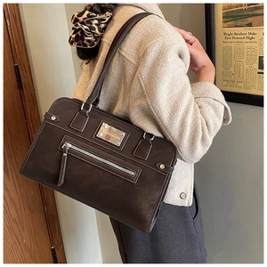 Détail d'un grand sac cabas en cuir mat marron avec fermeture éclair argentée et plaque