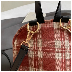 Detail of red-brown checkered fabric texture with black leather handle and gold hardware