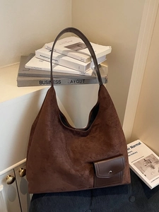 Retro brown suede tote bag with smooth leather strap leaning against classic books