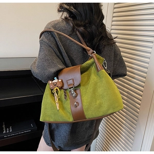 Detail view of large green tote bag with brown leather flap and bear charm on shoulder
