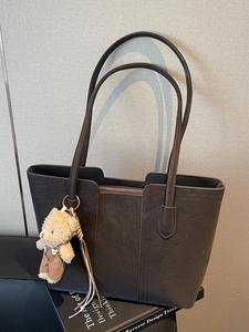 Minimalist large brown leather tote bag with plush bear charm and long shoulder strap