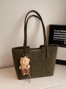 Olive green suede tote bag with plush bear charm in a minimalist studio setting