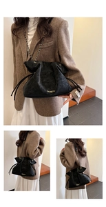 Detail of black matte bucket bag featuring gold fashion text and chain shoulder strap