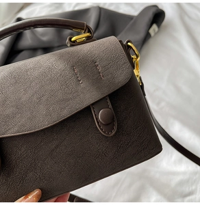 Detail of dark brown leather crossbody bag with pleated texture and gold metal hardware