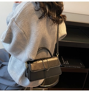 Vue détaillée d'un sac à bandoulière vintage en cuir noir avec détails dorés sur un pull