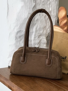 Brown faux suede shoulder bag with contrast stitching and dual zipper closure on a wooden table