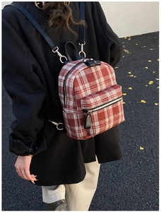 Macro detail of a red tartan plaid backpack with gold zipper and leather straps