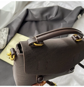 Close-up of deep brown textured leather handbag featuring gold metal hardware accents