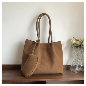 Detail of a brown suede tote bag with matching zipper pouch on a wooden shelf