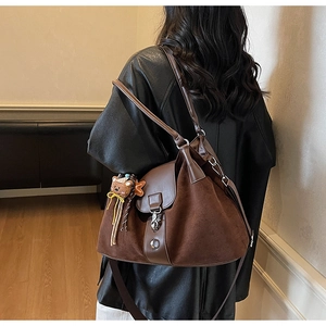 Detail of the large brown tote bag with leather flap and plush bear charm on a model