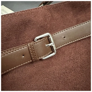 Détail d'un cabas en daim marron foncé avec boucle argentée et coutures précises