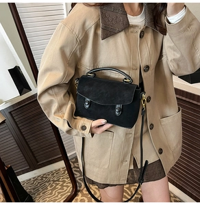 Detail of matte black crossbody bag with gold hardware and circular buckle on a model