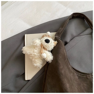 Detail of cute white plush bear charm with brown knit hat on a suede tote bag