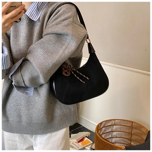 Dettaglio della borsa hobo nera con ciondolo circolare indossata da una modella
