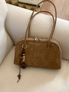 Retro brown faux suede shoulder bag with beaded charm on a soft cream sofa