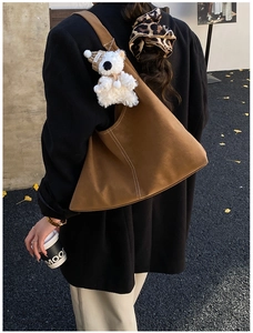 Detail of a brown suede hobo bag with contrast stitching and a plush bear charm on strap